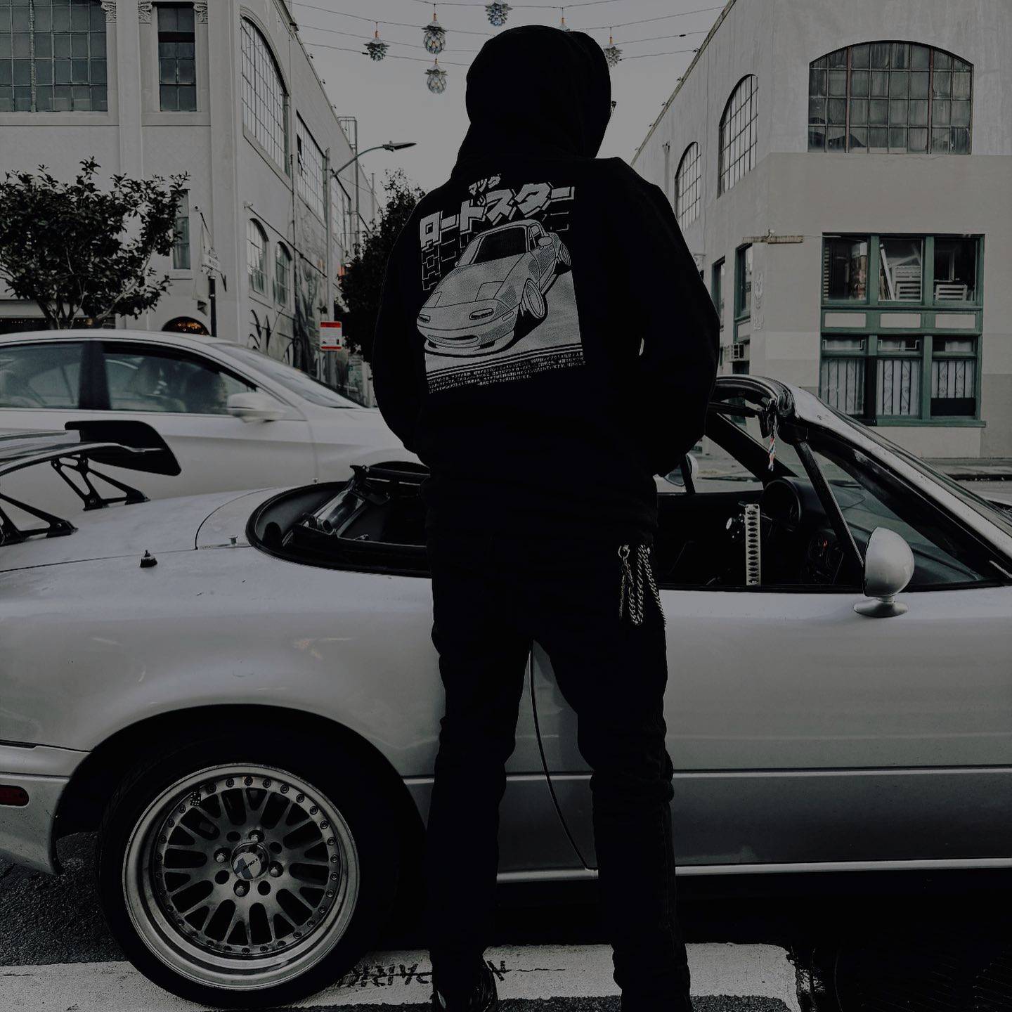 Person standing next to a car with a graphic design on their shirt, in an urban setting.