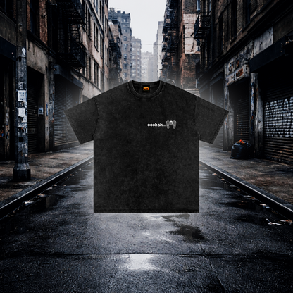 A black textured short-sleeve t-shirt with a small white horizontal bar graphic on the chest, floating over a wet, empty urban alleyway.