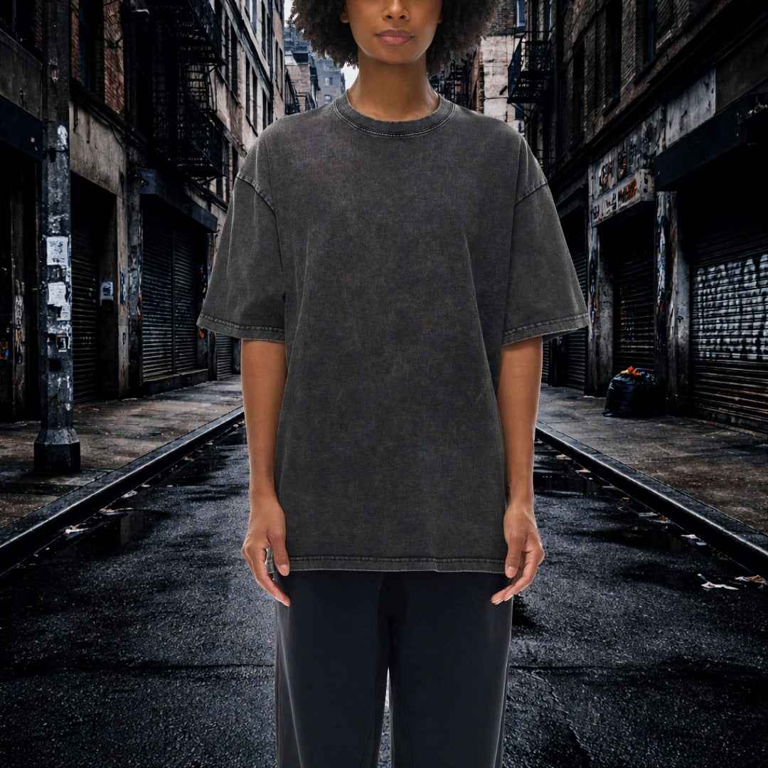 Person wearing a dark gray t-shirt and black pants standing in an urban alleyway.